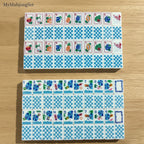 Blue gingham American mahjong tiles with colorful travel and beach vacation icons on a wooden surface