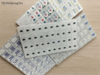 MyMahjongSet white pearl acrylic American mahjong tiles in shrink-wrapped stacks with colorful engraved symbols.