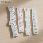 MyMahjongSet white pearl acrylic mahjong tiles with floral and numerical designs arranged on a wooden table.
