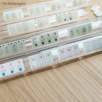 MyMahjongSet American mahjong tiles with a white pearl finish arranged on clear acrylic racks on a wooden table.