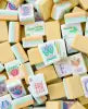 Yellow American Mahjong tiles with soft pastel artwork scattered across a table, featuring premium acrylic construction and an elegant custom design for American Mahjong players.